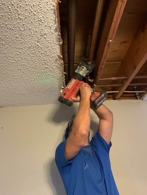 Technician working on plumbing pipe above a ceiling